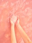 Female holding healing salt pile in hands in pink water — Stock Photo