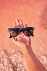 Female hand holding sunglasses above pink water — Stock Photo