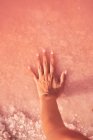 Frauenhand berührt heilenden Salzhaufen in rosa Wasser — Stockfoto