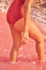 Обрізаний вид на засмажену жінку в купальнику, що виходить з рожевої води солоного озера в літній час — стокове фото
