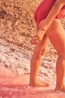 Cropped view of slender female in swimwear walking in pink salty water — Stock Photo