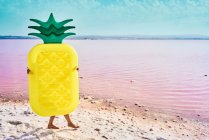 Donna che cammina sulla riva del mare coperta di materasso ad aria in forma di ananas in laguna rossa — Foto stock