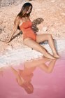 Тонка молода жінка в червоному купальнику відпочиває на солоному пляжі з рожевою водою — стокове фото