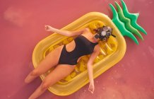Frau mit Atemschutzmaske liegt auf Luftmatratze im rosafarbenen Seewasser — Stockfoto