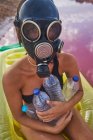Feminino em máscara de gás e com garrafas de plástico em água do lago — Fotografia de Stock