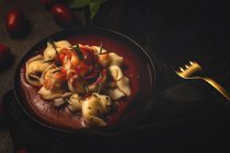 Raviolis cuits avec sauce tomate et herbes dans un bol à côté de la fourchette et serviette sur la table — Photo de stock
