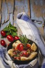 Ravioli cozido com molho de tomate e ervas na placa ao lado de tomates e pano na mesa rústica de madeira — Fotografia de Stock