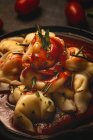Готовые равиоли с томатным соусом и травами в миске рядом с вилкой и салфеткой на столе — стоковое фото