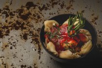 Варені равіолі з томатним соусом і травами в мисці поруч з виделкою і серветкою на столі — стокове фото