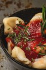 Raviolis cocidos con salsa de tomate y hierbas en un tazón junto a tenedor y servilleta en la mesa - foto de stock