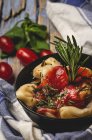 Raviolis cocidos con salsa de tomate y hierbas en plato junto a tomates y paño sobre mesa rústica de madera - foto de stock