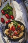 Ravioli cotti con salsa di pomodoro ed erbe aromatiche sul piatto accanto ai pomodori e stoffa sul tavolo rustico in legno — Foto stock