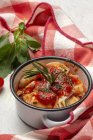Raviolis cuisinés avec sauce tomate et herbes sur une casserole de sauce casserole à côté de tomates sur un chiffon dans une table — Photo de stock