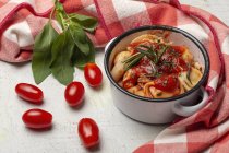Gekochte Ravioli mit Tomatensauce und Kräutern auf Saucenpfanne neben Tomaten auf Tuch auf einem Tisch — Stockfoto