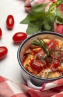 Gekochte Ravioli mit Tomatensauce und Kräutern auf Saucenpfanne neben Tomaten auf Tuch auf einem Tisch — Stockfoto