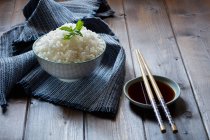 Ciotola di riso tradizionale giapponese su asciugamano grigio e bacchette su piattino con salsa di soia sul tavolo di legno . — Foto stock