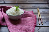 Bowl of traditional Japanese rice on pink towel and chopsticks on wooden table. — Stock Photo