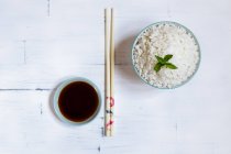 Bowl of traditional Japanese rice and chopsticks by saucer with soy sauce on white table. — Stock Photo