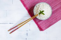 Schüssel mit traditionellem japanischen Reis auf rosa Handtuch und Essstäbchen auf weißem Tisch. — Stockfoto