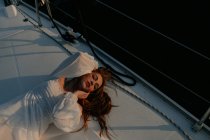 Relajada hermosa mujer acostada en el arco del barco y descansando mientras disfruta de viaje por mar con los ojos cerrados - foto de stock