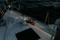 Belle femme détendue allongée sur la proue du navire et se reposant tout en profitant du voyage en mer avec les yeux fermés — Photo de stock