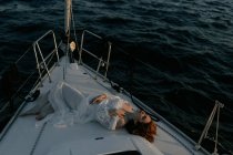 Relajada hermosa mujer acostada en el arco del barco y descansando mientras disfruta de viaje por mar con los ojos cerrados - foto de stock