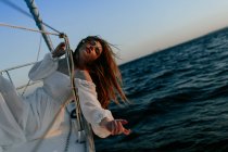 Транквіль жінка в розкішній білій сукні відпочиває, лежачи на яхті під час круїзу із закритими очима — стокове фото