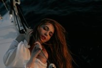 Ruhige Frau im weißen Luxuskleid, die während einer Kreuzfahrt mit geschlossenen Augen auf einer Jacht liegt — Stockfoto