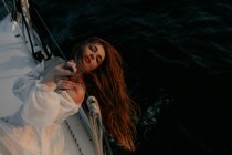 Спокойная женщина в роскошном белом платье отдыхает на яхте во время круиза с закрытыми глазами — стоковое фото