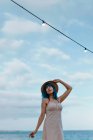 Femme inspirée aux cheveux bleus en chapeau et robe de soleil flânant le long d'un quai en béton au bord d'une mer colorée — Photo de stock
