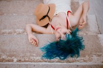 Мрійлива жінка з барвистим блакитним волоссям в сараї, що лежить на кам'яних сходах — стокове фото