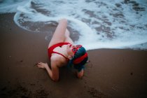 Модна жінка з блакитним волоссям в червоному яскравому купальнику насолоджується лежачи на піщаному пляжі — стокове фото