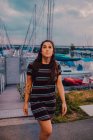 Bonne jeune femme tatouée en robe qui marche le long d'un quai rempli de yachts et de bateaux — Photo de stock