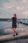 Bonne jeune femme tatouée en robe debout sur un quai rempli de yachts et de bateaux — Photo de stock