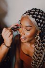 Attractive Femme adulte noire appliquant l'ombre aux yeux d'un maquilleur professionnel en studio — Photo de stock