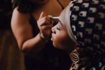 Atraente fêmea adulta preta aplicando sombra ocular de maquiador profissional em estúdio — Fotografia de Stock