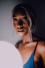 Attraktive erwachsene schwarze Frau mit weißem Luftballon in der Dunkelheit, die in die Kamera blickt — Stockfoto