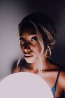 Mulher adulta negra atraente com balão branco iluminado na escuridão olhando para a câmera — Fotografia de Stock