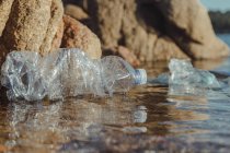 Resíduos de garrafas enrugadas de plástico vazios deitados em água limpa à beira-mar perto de rochas — Fotografia de Stock