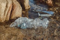 Bottiglie vuote di plastica accartocciate rifiuti che giacciono in acqua limpida sul mare vicino alle rocce — Foto stock