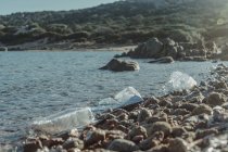 Пустые пластиковые скомканные бутылки отходы лежат на прибрежной скале рядом с чистой водой — стоковое фото