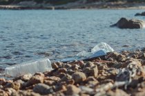 Empty plastic crumpled bottles waste lying on the seaside rock near clear water — Stock Photo