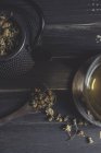 De arriba de la margarita seca en la cuchara a la mesa oscura de madera cerca de la taza con el té de hierbas - foto de stock