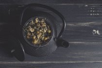 Montón de margaritas secas para hacer té en tetera de metal sobre mesa oscura - foto de stock