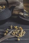 Сверху сушеная маргаритка в ложке на темном деревянном столе возле чашки с травяным чаем — стоковое фото
