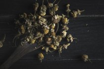 Gros plan de tas de marguerites séchées dans une cuillère en bois sur une table noire pour la fabrication du thé — Photo de stock