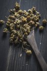 Gros plan de tas de marguerites séchées dans une cuillère en bois sur une table noire pour la fabrication du thé — Photo de stock
