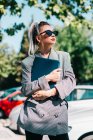 Businesswoman with trendy hairstyle sunglasses and suit holding laptop and looking away in parking lot at bright day — Stock Photo