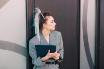 Empresária com penteado na moda e terno segurando laptop e olhando para longe na parede — Fotografia de Stock