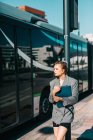 Модная деловая женщина, держащая планшет в костюме и солнцезащитных очках, опираясь на автобусную остановку и отворачиваясь — стоковое фото